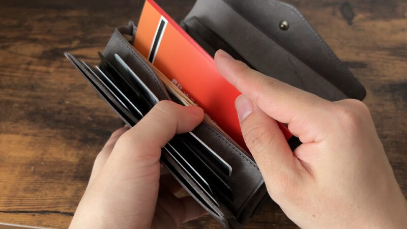 STUDIUM(ストゥディウム)のスタンドアップウォレットの札入れに通帳を入れているシーン